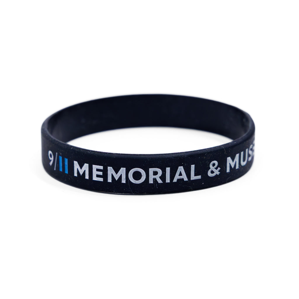 A black rubber bracelet with the inscriptions 'HONOR AND REMEMBER' and '9/11 MEMORIAL' in white and blue letters.