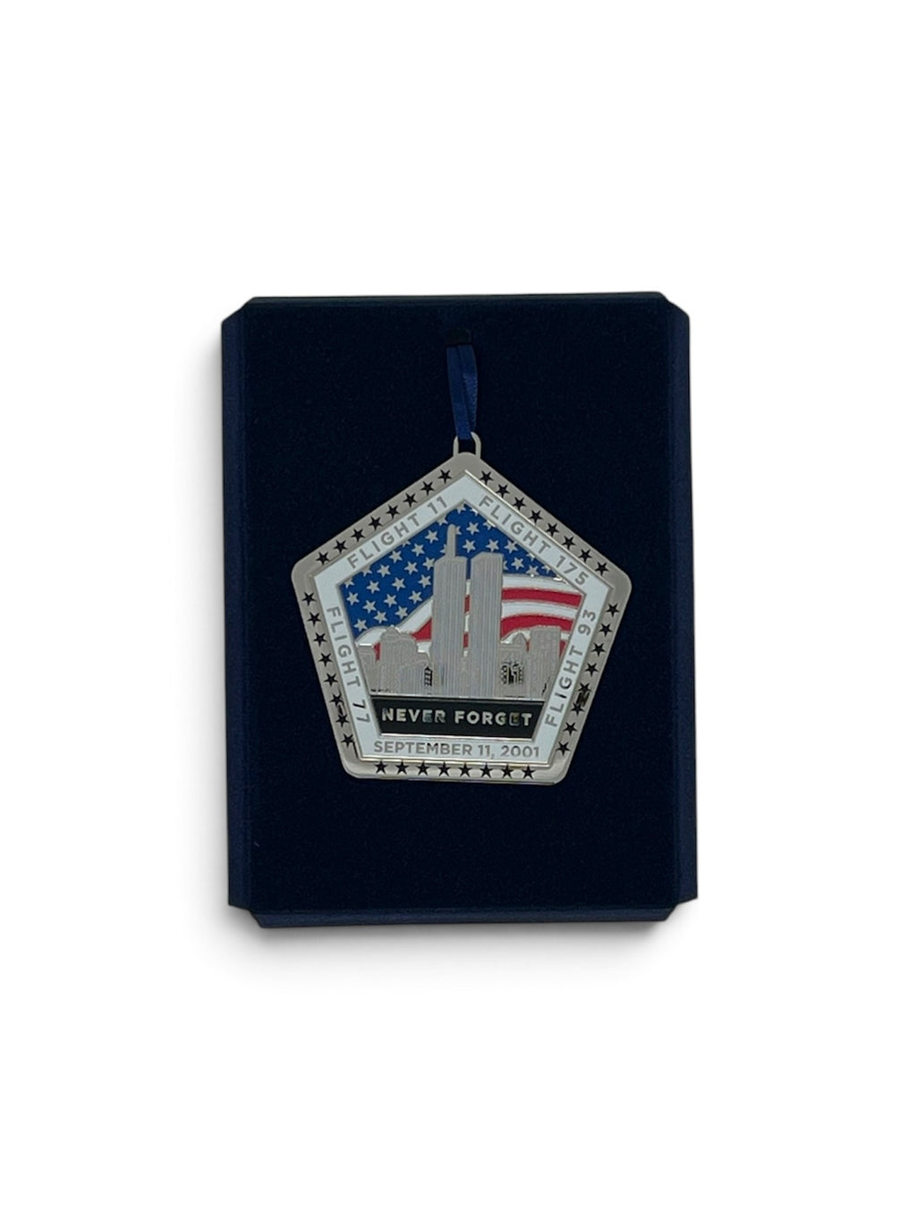 A pentagonal commemorative hanging ornament displayed on a dark navy presentation card against a white background. The ornament features the Twin Towers, an American flag, stars, and the text 'NEVER FORGET' and 'SEPTEMBER 11, 2001'.