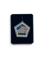 A pentagonal commemorative hanging ornament displayed on a dark navy presentation card against a white background. The ornament features the Twin Towers, an American flag, stars, and the text 'NEVER FORGET' and 'SEPTEMBER 11, 2001'.