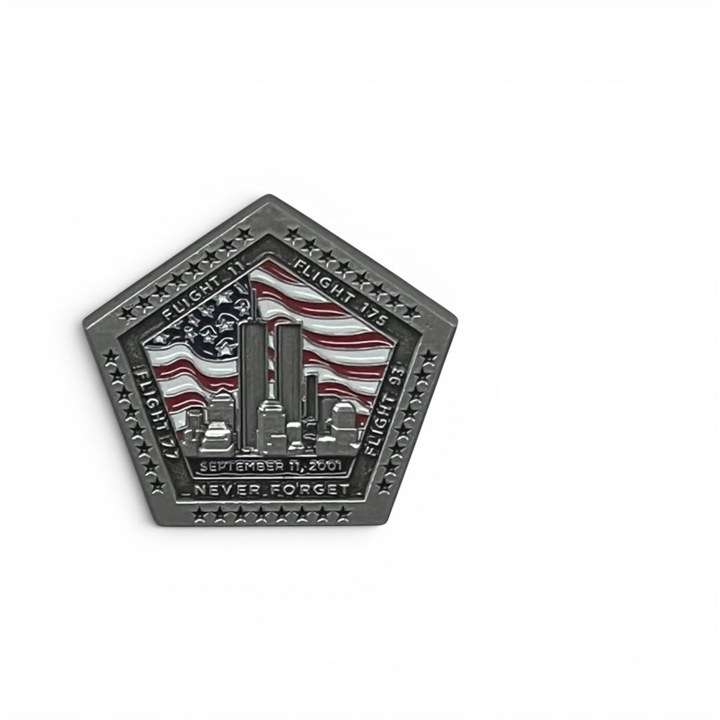 A pentagonal commemorative pin in a dark matte silver finish, featuring an American flag and the New York City skyline with the towers. The flight numbers and  text reading 'SEPT 11 2001', and 'NEVER FORGET' is engraved around the border.