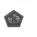 A pentagonal commemorative pin in a dark matte silver finish, featuring an American flag and the New York City skyline with the towers. The flight numbers and  text reading 'SEPT 11 2001', and 'NEVER FORGET' is engraved around the border.