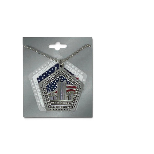 A silver-toned 9/11 memorial pendant necklace on a ball chain, displayed on a gray retail backing card. The pendant features a pentagonal design with the Twin Towers, stars, and red, white, and blue American flag details, plus the text 'NEVER FORGET' and 'SEPTEMBER 11, 2001'.