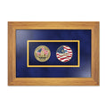 A framed commemorative display featuring two circular coins on a dark blue mat inside a light brown wood frame. The left coin shows the Twin Towers with the American Flag and the right coin features an American flag design and the 9/11 Memorial & Museum logo.