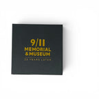 A black square box with gold lettering that reads '9/11 MEMORIAL & MUSEUM 25 YEARS LATER' on a plain white background.
