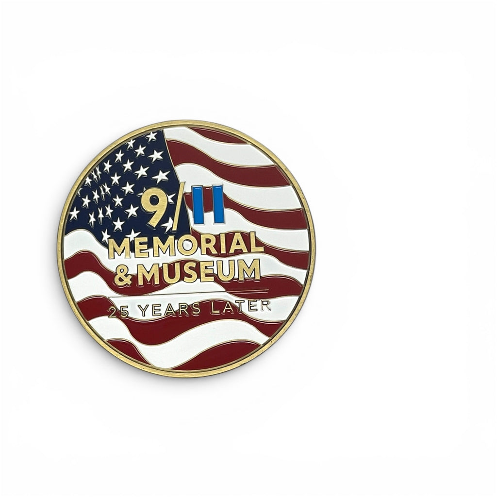 A circular coin featuring a stylized American flag with gold text reading '9/11 Memorial & Museum' and '25 Years Later' on a white background.