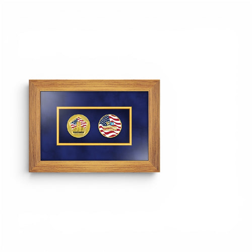 A framed wall art piece featuring two circular medallion coins on a dark blue background, enclosed in a light brown wood frame. The left emblem is gold with a red, white, and blue American flag design and the text 'NEVER FORGET'; the right emblem is red, white, and blue with a gold border and the text '9/11 Memorial & Museum'.