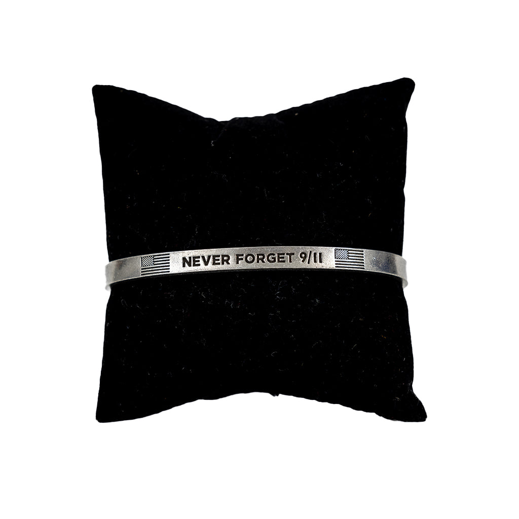 A silver pewter cuff bracelet with the inscription 'NEVER FORGET 9/11' on a black cushion.