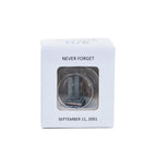 A glass keepsake ornament with a gold-colored cord, containing a miniature replica of the Twin Towers in a small grey square box with the words 'NEVER FORGET' and 'SEPTEMBER 11, 2001'.