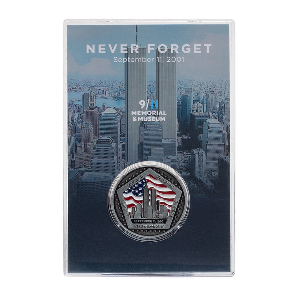A commemorative coin with a US flag and Twin Towers design, housed in a clear display case, with 'NEVER FORGET' text on the case.