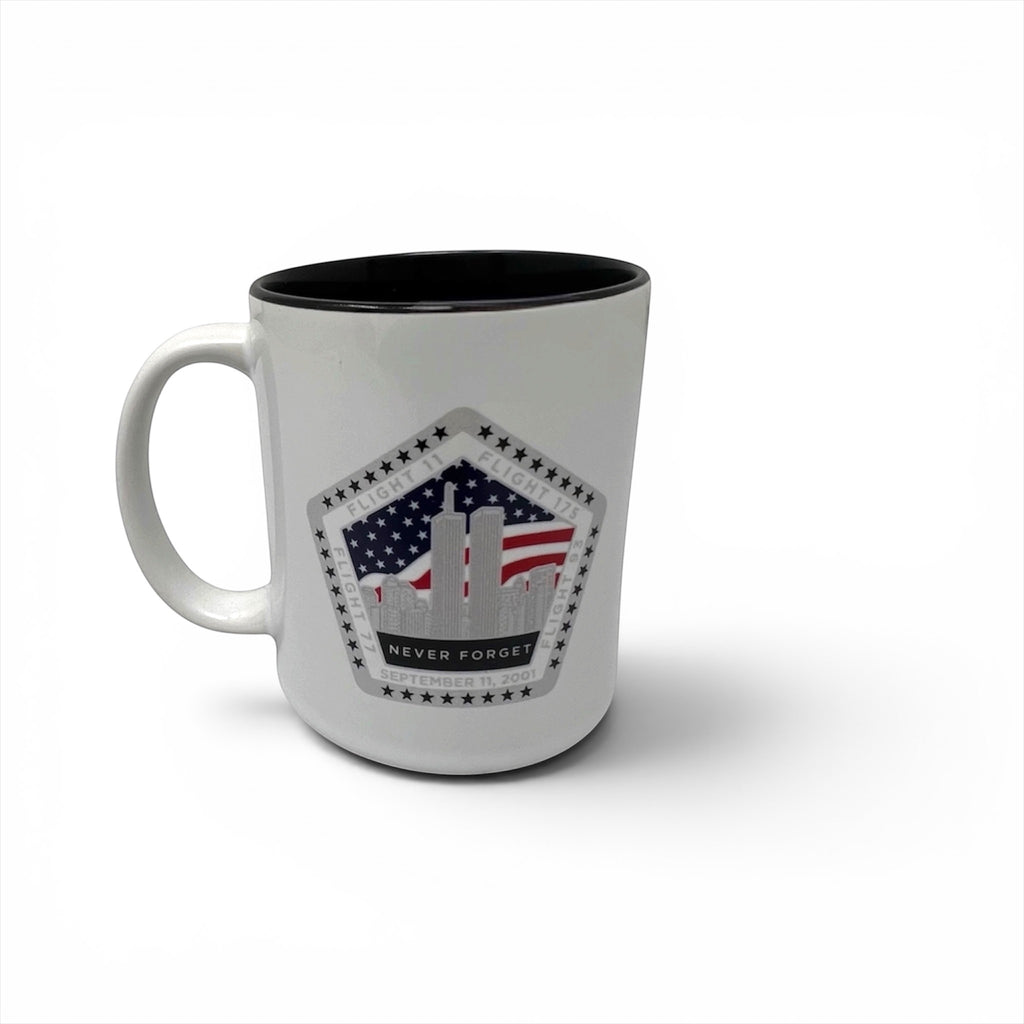 A white ceramic mug with a black interior, featuring a printed graphic on the front of the Twin Towers silhouette with an American flag background and the words 'NEVER FORGET'.