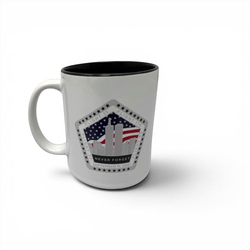 A white ceramic mug with a black interior, featuring a printed graphic on the front of the Twin Towers silhouette with an American flag background and the words 'NEVER FORGET'.