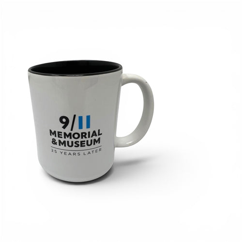 A white ceramic mug with a black interior, featuring the text '9/11 MEMORIAL & MUSEUM 25 YEARS LATER' printed in black and blue, set against a plain white background.