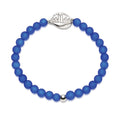 A beaded stretch bracelet made of matte royal blue beads, featuring a silver-toned metal NEVER FORGET medallion and a small silver accent bead, shown on a plain white background.
