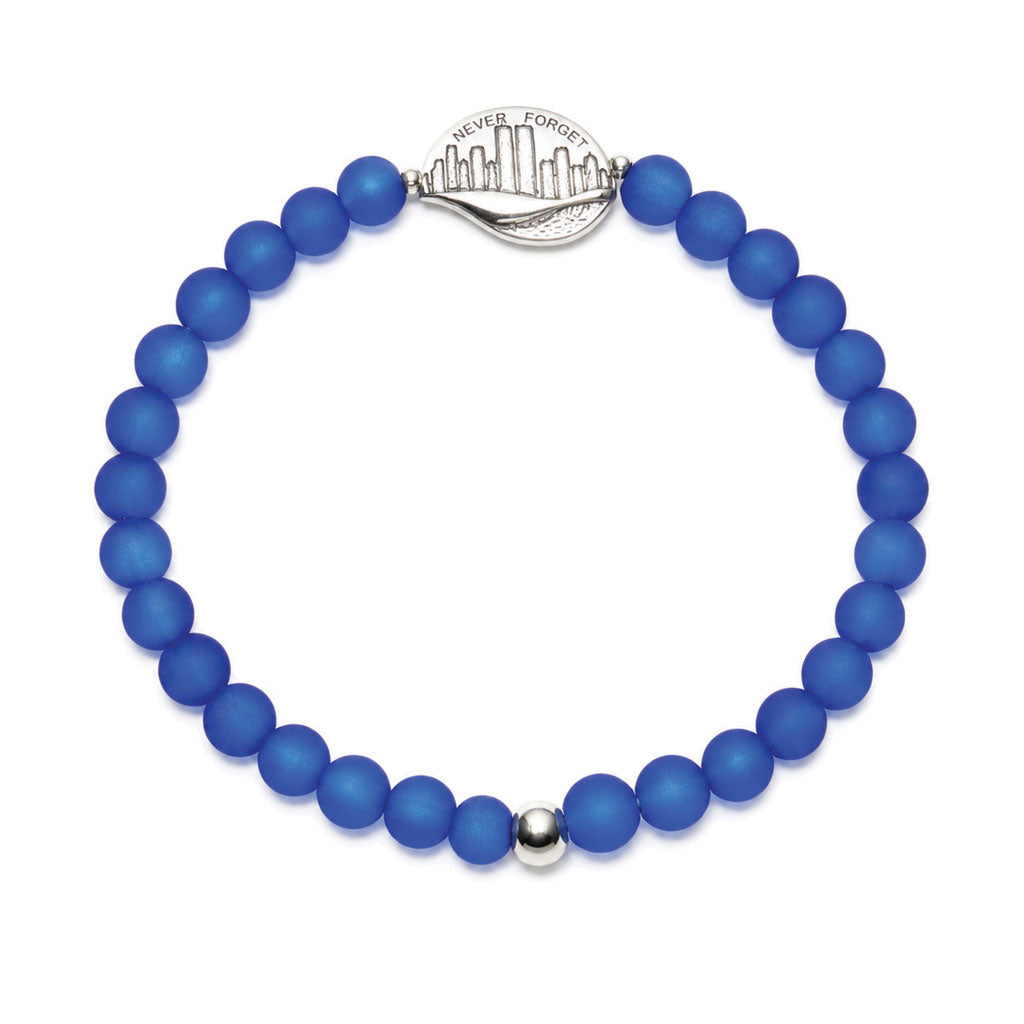 A beaded stretch bracelet made of matte royal blue beads, featuring a silver-toned metal NEVER FORGET medallion and a small silver accent bead, shown on a plain white background.