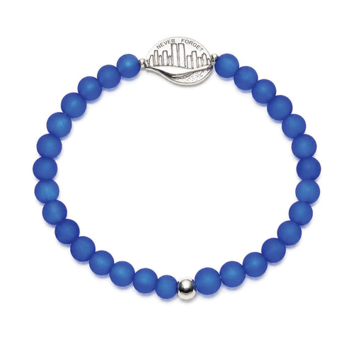 A beaded stretch bracelet made of matte royal blue beads, featuring a silver-toned metal NEVER FORGET medallion and a small silver accent bead, shown on a plain white background.