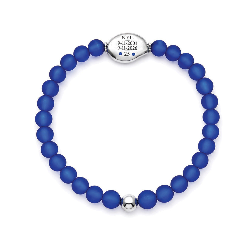 A beaded stretch bracelet made of matte royal blue beads with a polished silver-toned oval centerpiece engraved with 'NYC 9-11-2001 9-11-2026 25', shown on a plain white background.