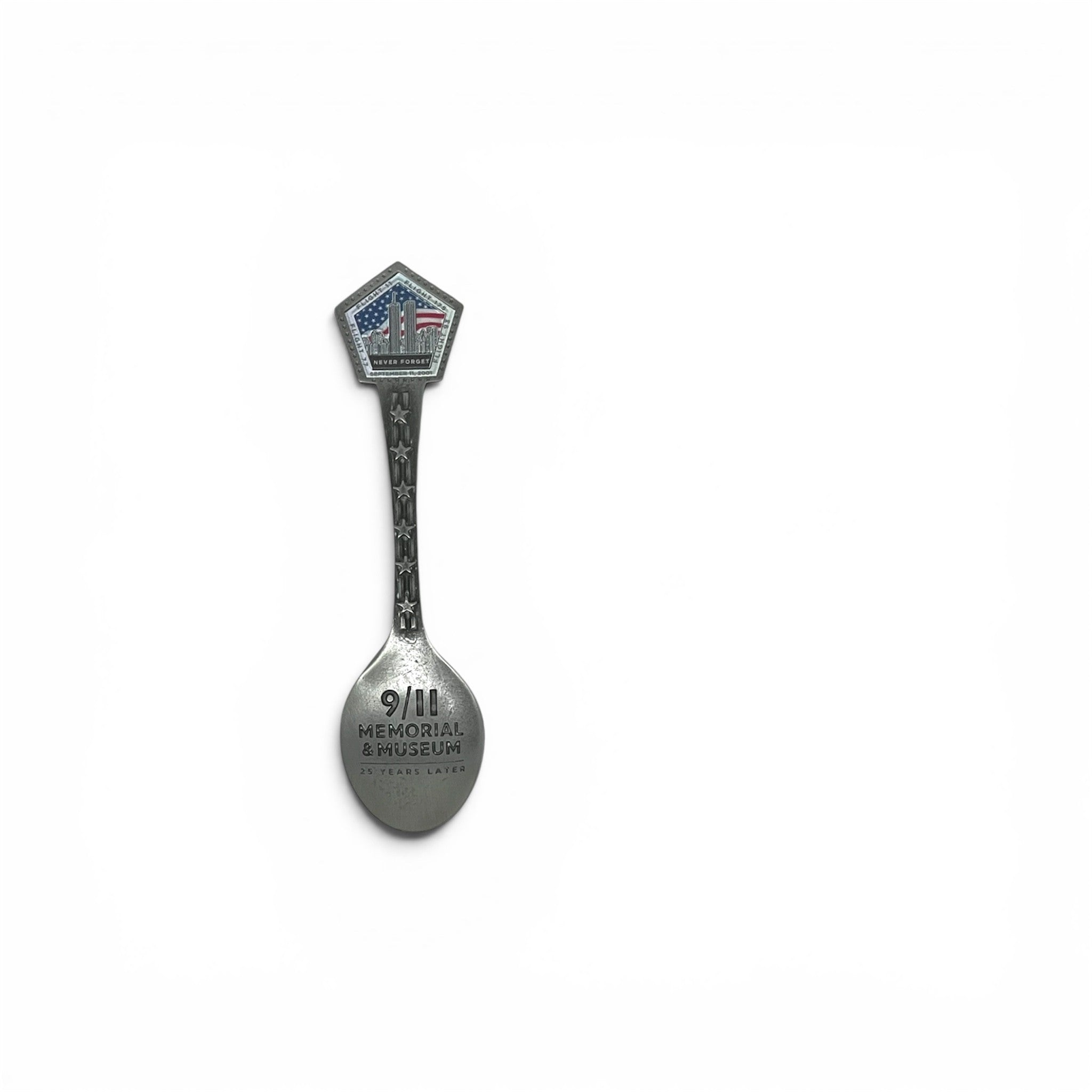 A silver-toned metal commemorative spoon with a pentagonal handle featuring an American flag design, and the words '9/11 MEMORIAL & MUSEUM' engraved on the spoon bowl, shown on a plain white background.