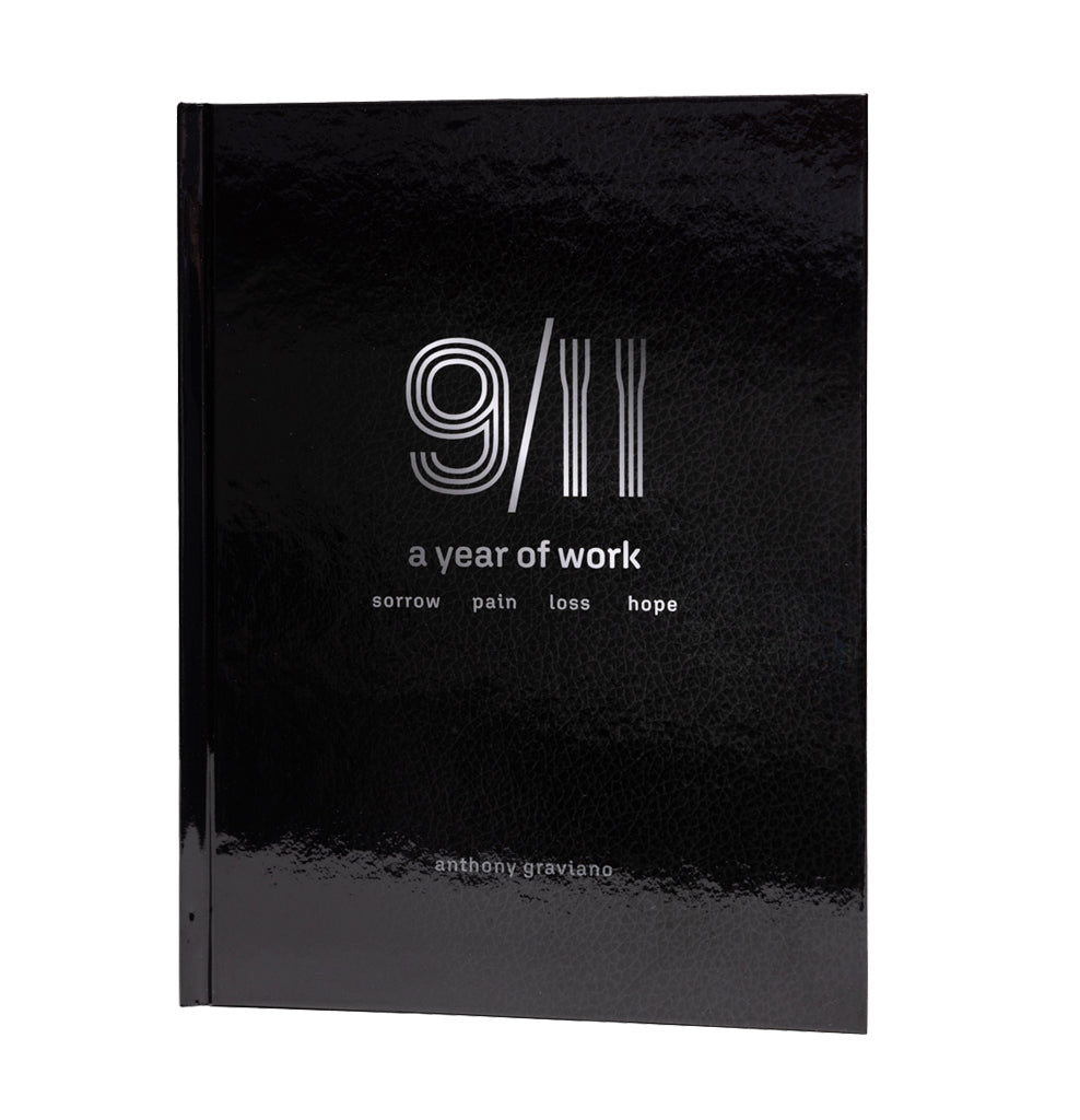 This image features the hardcover book titled "9/11: A Year of Work" by Anthony Graviano. The cover is a striking black, with minimalistic white and grey text and graphics that evoke a sense of somber reflection.