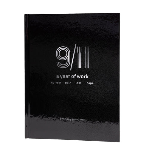 This image features the hardcover book titled "9/11: A Year of Work" by Anthony Graviano. The cover is a striking black, with minimalistic white and grey text and graphics that evoke a sense of somber reflection.