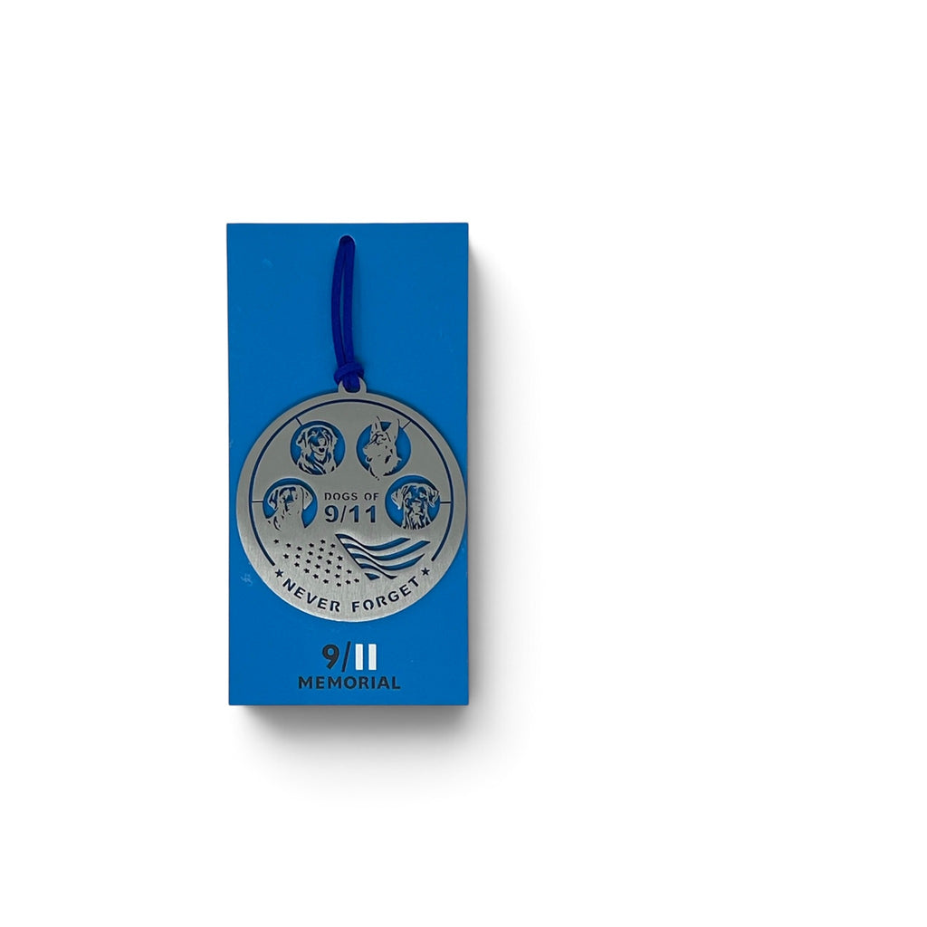 A round silver-toned metal memorial ornament with a blue hanging cord, featuring four rescue dog emblems and the words 'Dogs of 9/11' and 'NEVER FORGET'.