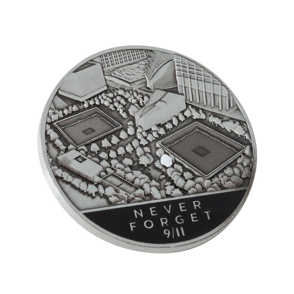 A collectible silver coin, with an aerial image of the Memorial Plaza and the inscription 'NEVER FORGET 9/11' 