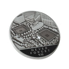 A collectible silver coin, with an aerial image of the Memorial Plaza and the inscription 'NEVER FORGET 9/11' 