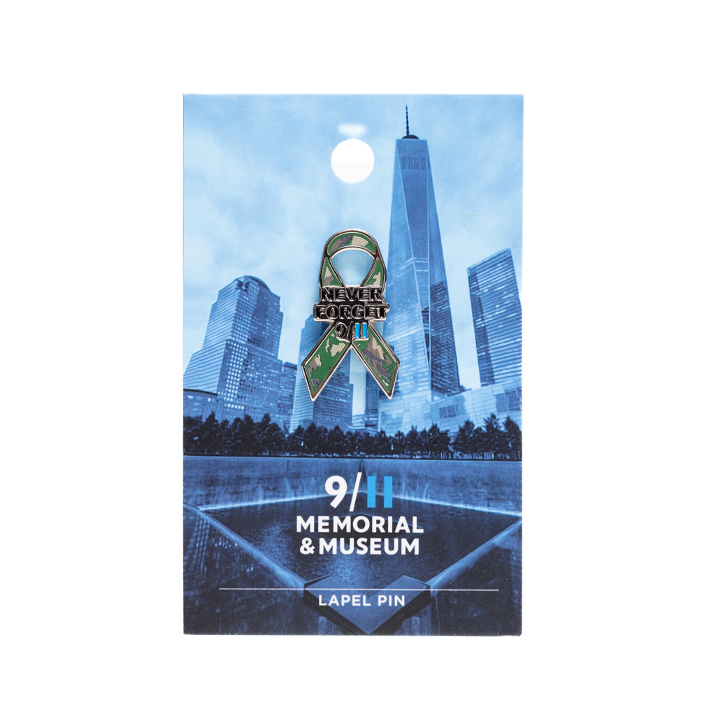 A camouflage ribbon lapel pin with the text 'NEVER FORGET 9/11' on a blue card backer.