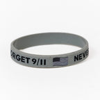 A grey rubber bracelet with the text 'NEVER FORGET 9/11', American Flag and Skyline printed on it.