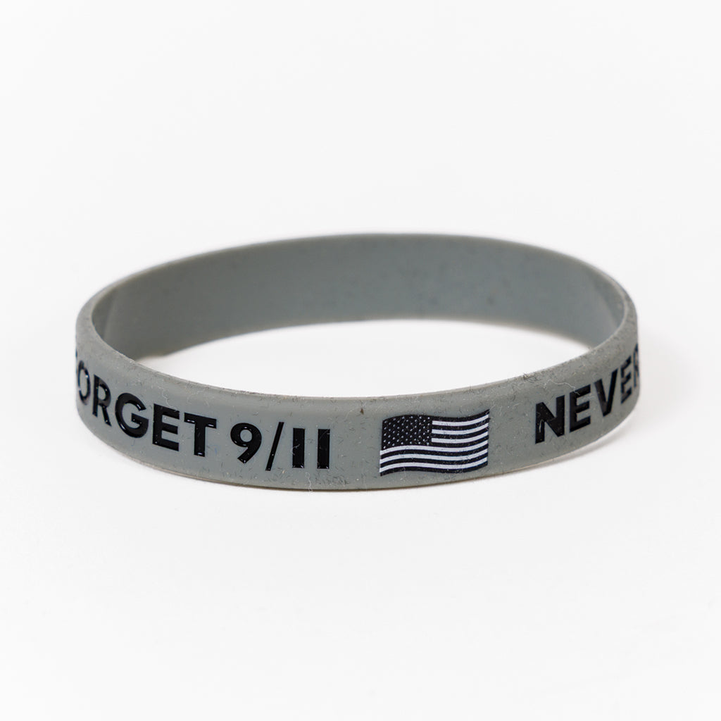 A grey rubber bracelet with the text 'NEVER FORGET 9/11', American Flag and Skyline printed on it.