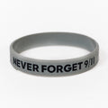 A grey rubber bracelet with the text 'NEVER FORGET 9/11', American Flag and Skyline printed on it.