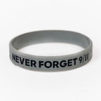 A grey rubber bracelet with the text 'NEVER FORGET 9/11', American Flag and Skyline printed on it.