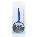 A stainless steel circular keepsake with an engraved image of three dogs and a flag with a blue ribbon attached on a white to blue omber card backer.