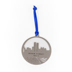 A stainless steel circular keepsake with a skyline silhouette and the text 'NEVER FORGET 9/11' inscribed on it, attached to a blue ribbon.