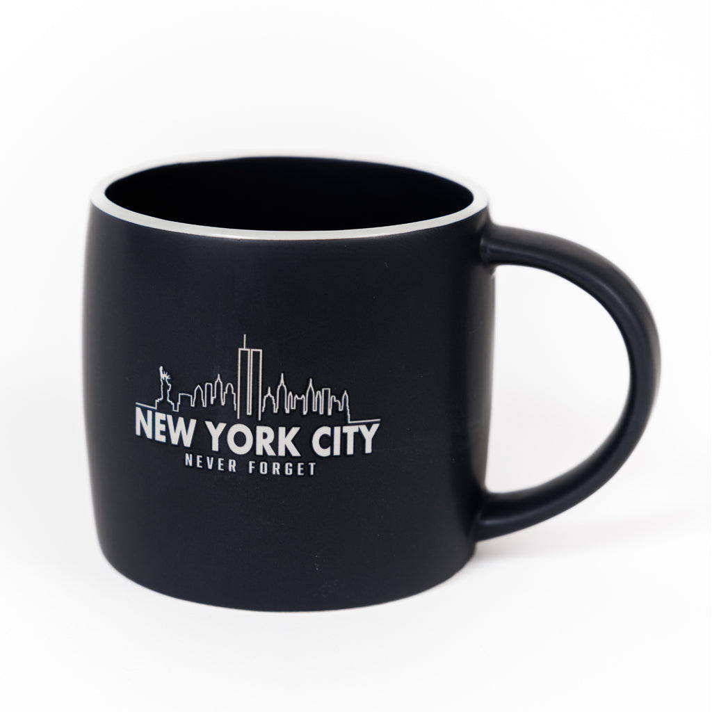 A black ceramic mug with 'NEW YORK CITY NEVER FORGET' text and a skyline etching.