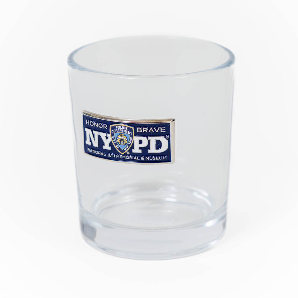 A clear water glass with the NYPD (New York Police Department) logo and the text 'Honor & Brave' and National 9/11 Memorial & Museum' printed on it.