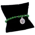 Green beaded bracelet with a silver tree of life charm on a black pillow