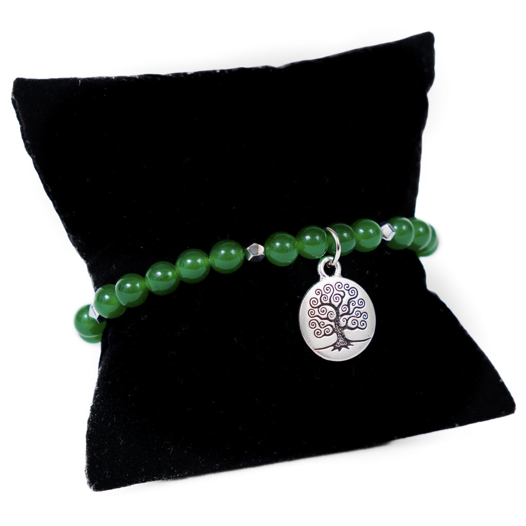 Green beaded bracelet with a silver tree of life charm on a black pillow