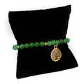 Green beaded bracelet with a gold tree of life charm on a black pillow