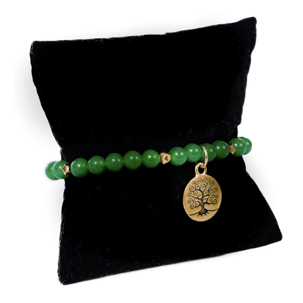 Green beaded bracelet with a gold tree of life charm on a black pillow