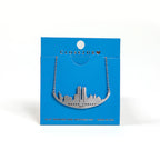 A stainless steel necklace with a skyline silhouette and the text 'NEVER FORGET 9/11' inscribed on it, on a blue card backer.