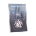 A commemorative coin with a US flag and Twin Towers design, housed in a clear display case, with 'NEVER FORGET' text on the case.