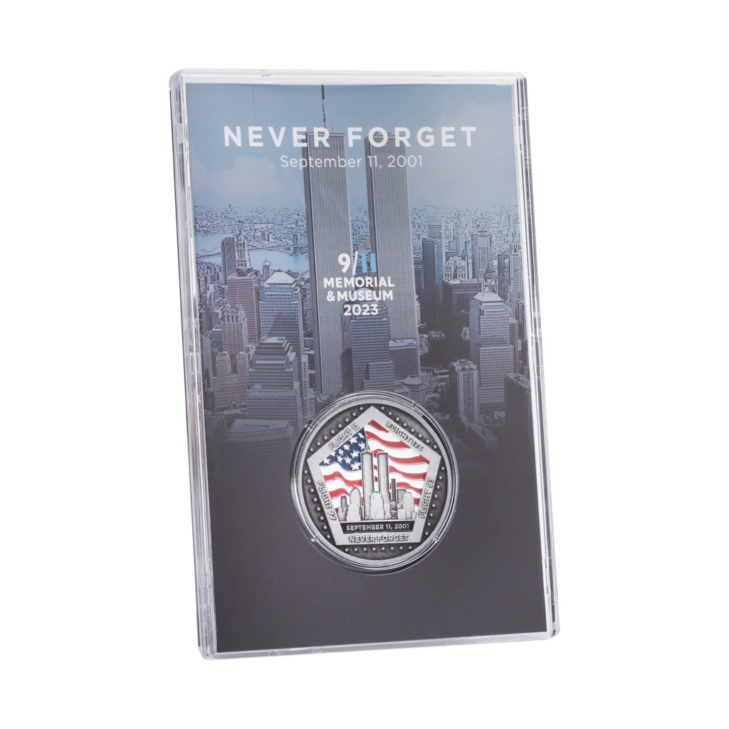 A commemorative coin with a US flag and Twin Towers design, housed in a clear display case, with 'NEVER FORGET' text on the case.