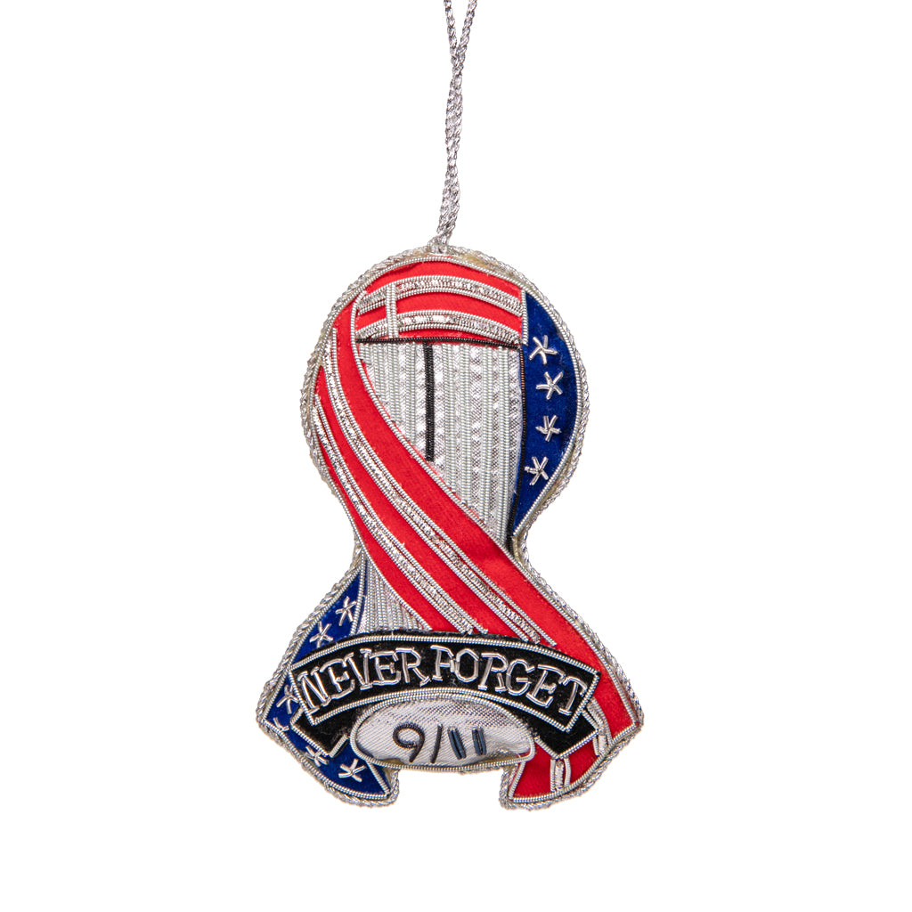 A plush keepsake in the shape of a ribbon with an American flag design and 'Never Forget 9/11' text, suspended by metallic loop.