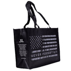 A black tote bag with a grey American flag design and the text 'NEVER FORGET 9/11' on it with the 9/11 Memorial logo and mission-based text on the side gusset.